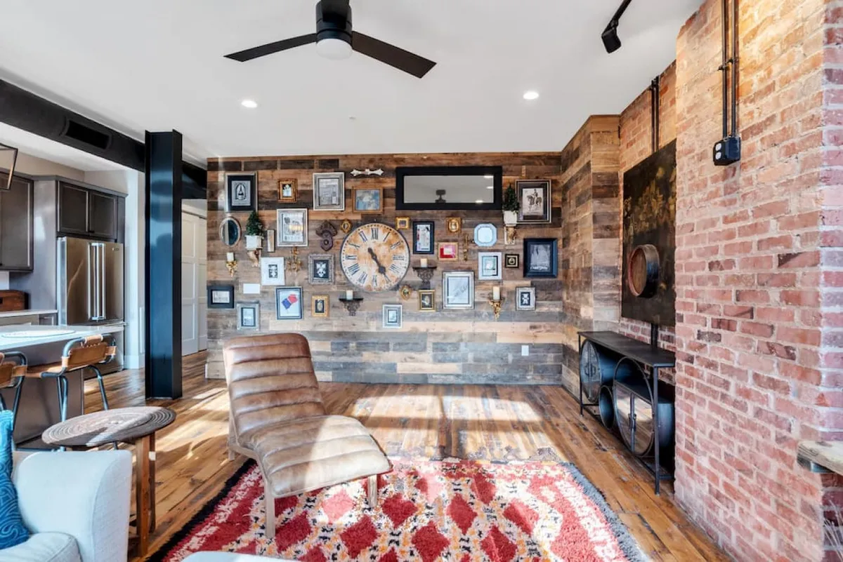 A cozy, eclectic sitting area with a gallery wall decorated with various frames and a clock, a unique seating chair, and a textured area rug. The room blends modern and rustic touches, offering a comfortable spot to relax or plan your city excursions.