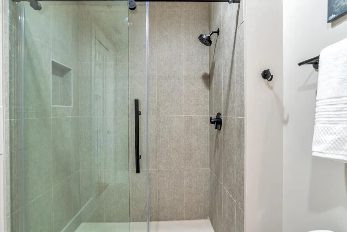 A sleek, modern bathroom featuring a glass shower enclosure, black fixtures, textured tile walls, and a neatly arranged towel rack. The ambiance is refreshing, clean, and perfectly suited to indulgent self-care routines.