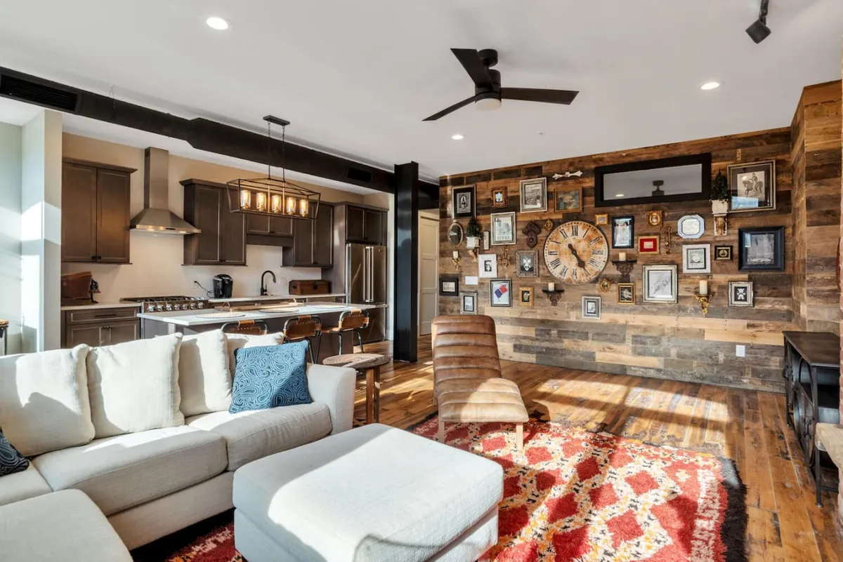 An inviting open-plan living area with a kitchen island, a comfortable sofa, a gallery wall of art, and a prominent clock. The kitchen is seamlessly integrated into the space, making it ideal for socializing and shared meals.
