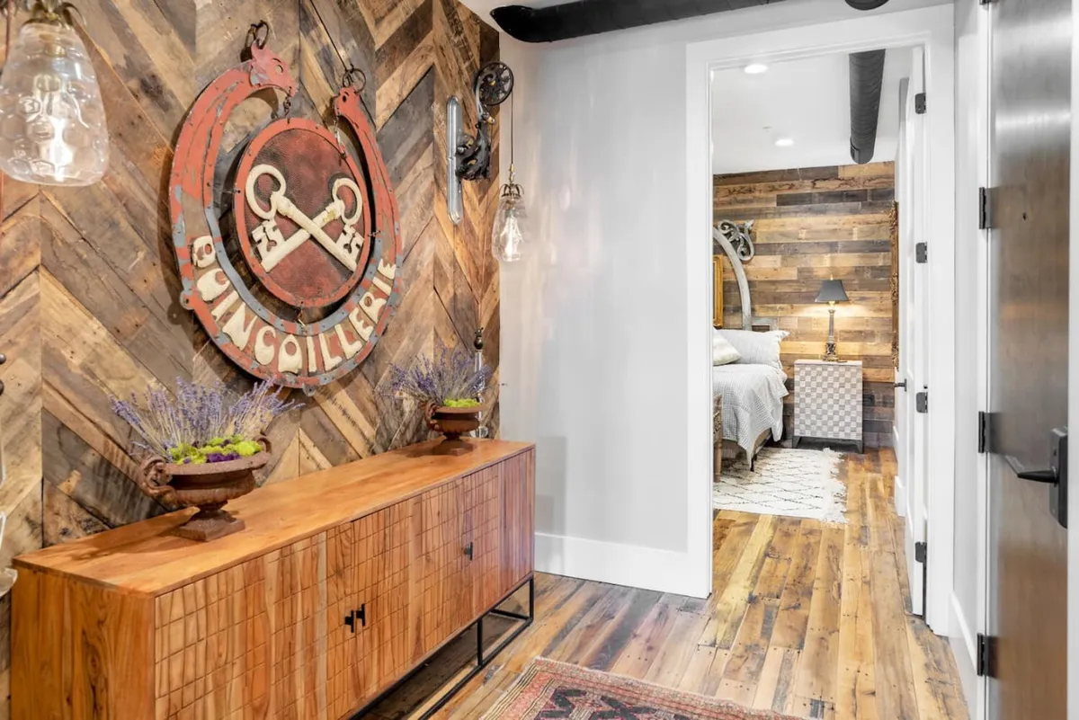 An inviting entryway with a distinctive wooden herringbone wall, a decorative 'keys' sign, and a stylish console table topped with a lavender arrangement. The ambiance is welcoming and modern, setting the tone for a comfortable stay downtown.
